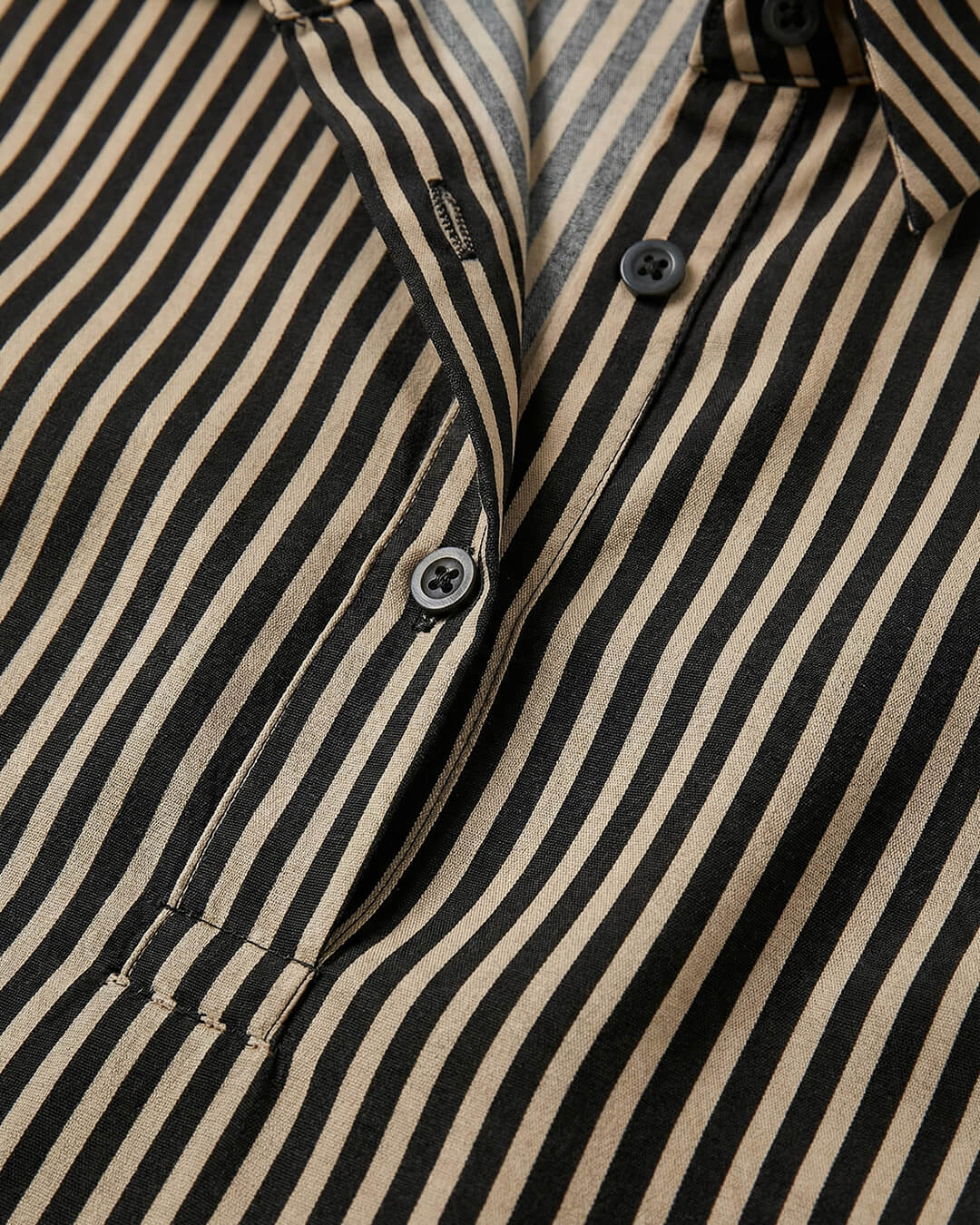Close-up of a black and beige striped shirt with buttons.- sfosh